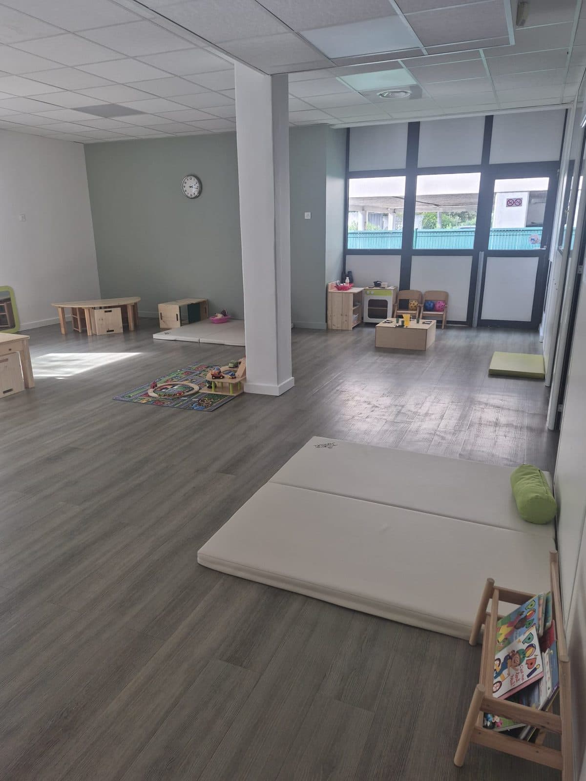 La grande salle de vie d'Aix-les-Milles : tapis de motricité, coin lecture, cuisinette et grandes baies vitrées